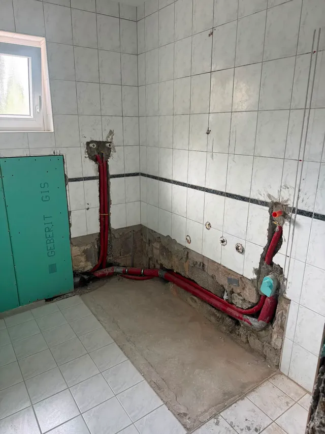 Rückbau im Bad: neue Leitungen in Schutzrohren laufen in Wandschlitzen und entlang des Bodens zur künftigen Duschecke