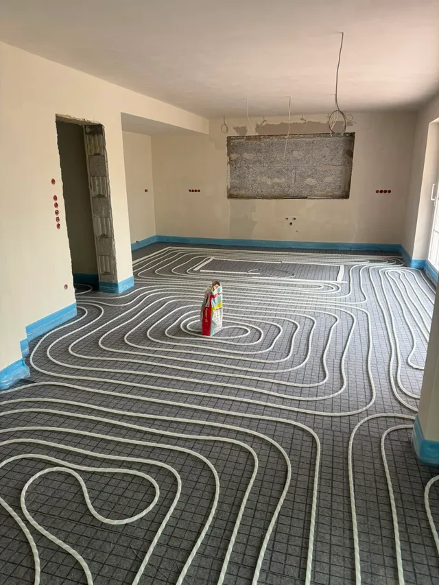 Weiterer Raum mit fertig verlegten Heizschleifen und blauem Randdämmstreifen an allen Wänden