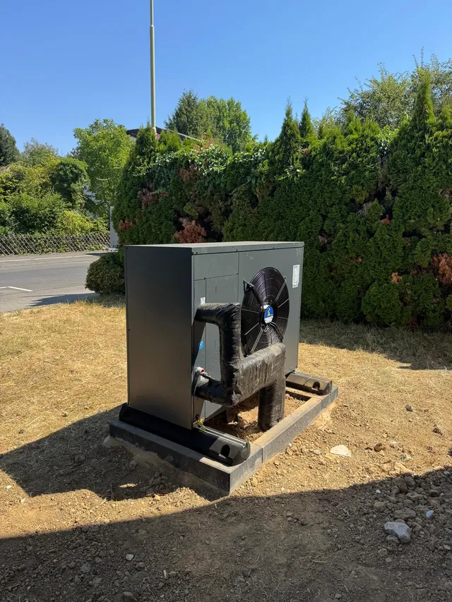 Außeneinheit derselben Wärmepumpe aus einem anderen Blickwinkel, freistehend mit Abstand zur Hecke