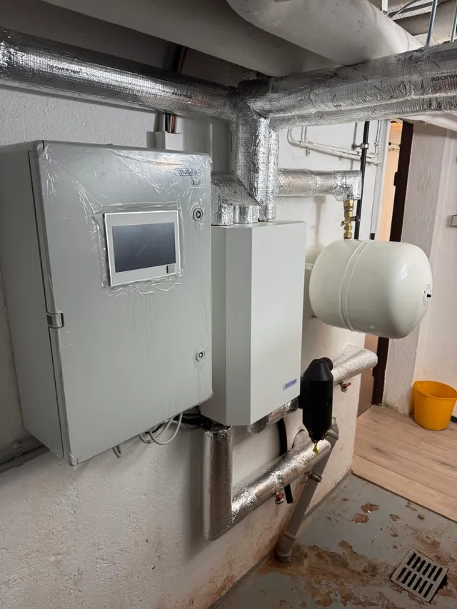 Hydraulikmodul der Wärmepumpe mit Schaltschrank und Regelungsdisplay, daneben Ausdehnungsgefäß und Schlammabscheider